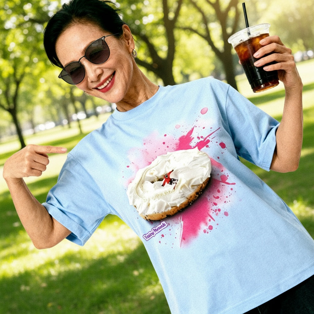 A beautiful asian female in her early 40s who is modeling a Tastey Threads  Backcountry Bagel super soft suaded shirt in powder blue.   The design consistsof a cream cheesed on a bagel, but the cream cheese is doubling as beautiful snow while a snowboarder is having a great time shredding